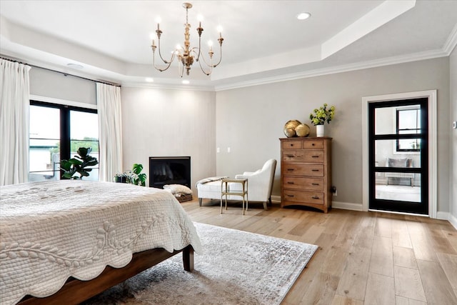 bedroom featuring ornamental molding, a chandelier, light wood-type flooring, and a tray ceiling