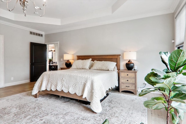 bedroom with hardwood / wood-style flooring, ornamental molding, a raised ceiling, and a chandelier