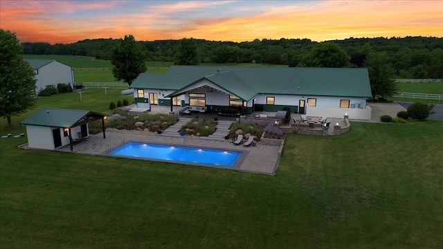 back house at dusk featuring a gazebo, a patio area, an outdoor structure, and a lawn