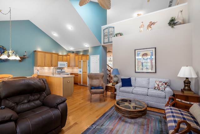 living room featuring ceiling fan, light hardwood / wood-style floors, sink, and high vaulted ceiling