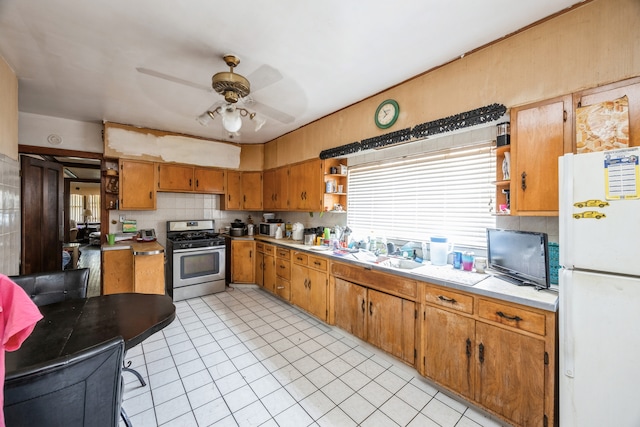 kitchen featuring tasteful backsplash, white refrigerator, light tile patterned floors, stainless steel gas range oven, and ceiling fan