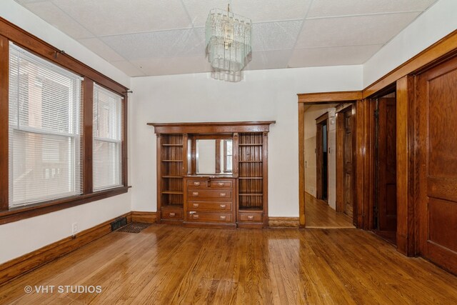 empty room featuring a paneled ceiling, wood-type flooring, and a notable chandelier