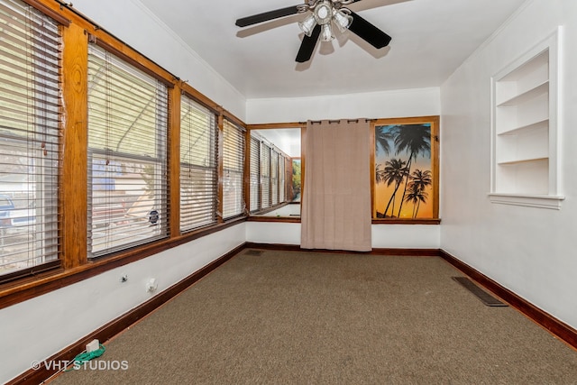 empty room featuring built in features, carpet flooring, ceiling fan, and crown molding