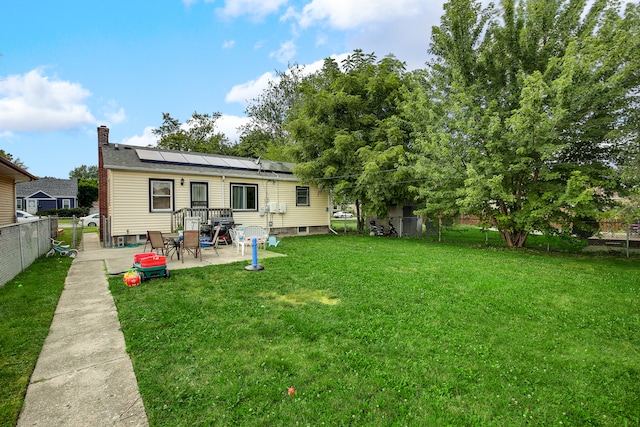 rear view of house with solar panels, a patio area, and a lawn