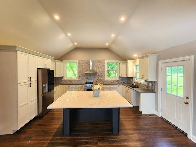 kitchen featuring appliances with stainless steel finishes, wall chimney range hood, sink, a center island, and dark wood-type flooring