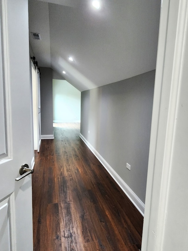 corridor featuring a textured ceiling, hardwood / wood-style flooring, lofted ceiling, and a barn door