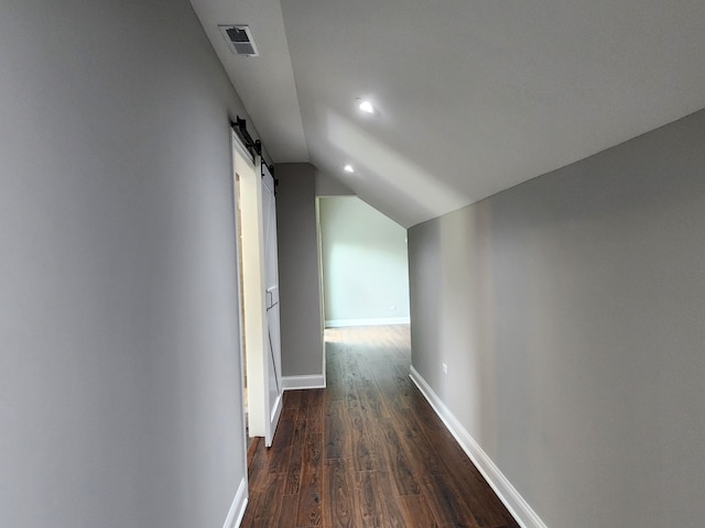 hallway featuring dark wood-type flooring, vaulted ceiling, and a barn door