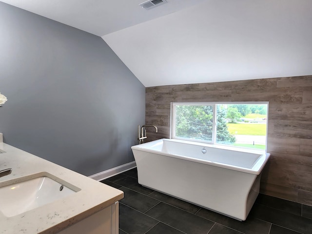 bathroom with tile patterned floors, vaulted ceiling, a bath, and vanity