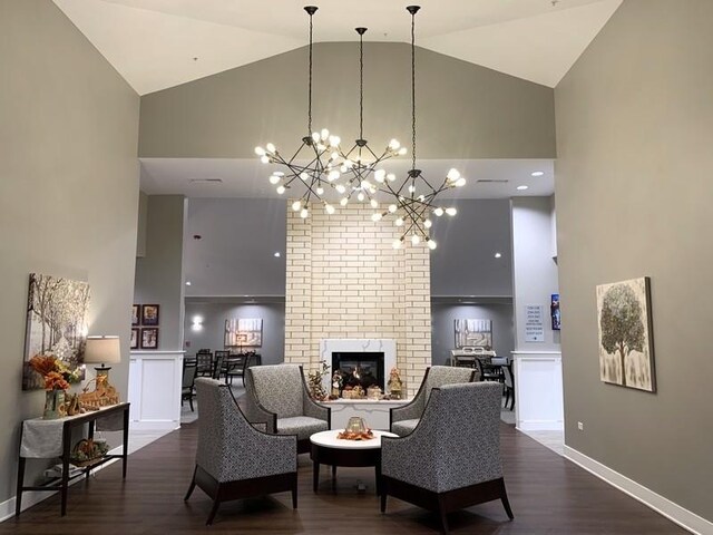 living room with a notable chandelier, high vaulted ceiling, brick wall, a brick fireplace, and dark wood-type flooring