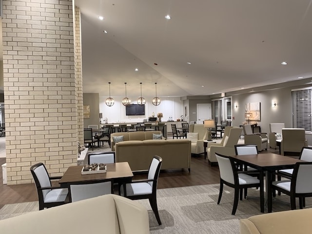 dining space with brick wall, wood-type flooring, and high vaulted ceiling