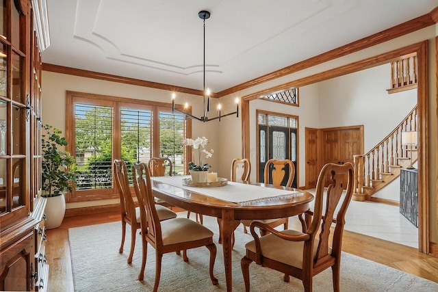 dining space with a notable chandelier, light wood finished floors, stairway, and crown molding