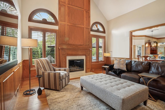 living room with a tile fireplace, a wainscoted wall, light wood-style flooring, and an inviting chandelier