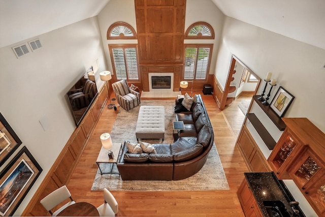 living room featuring high vaulted ceiling, a tile fireplace, visible vents, and light wood-style floors