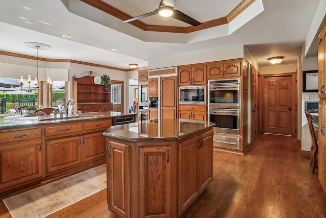 kitchen with a tray ceiling, brown cabinets, a sink, and built in appliances