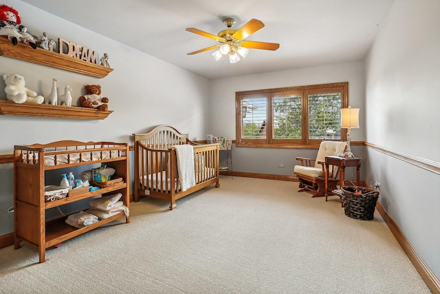 carpeted bedroom with a nursery area, ceiling fan, and baseboards