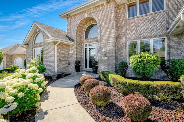 view of exterior entry with a shingled roof and brick siding