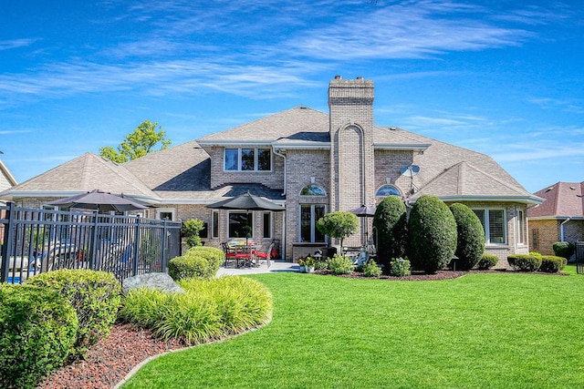 rear view of house featuring brick siding, fence, a yard, a chimney, and a patio area