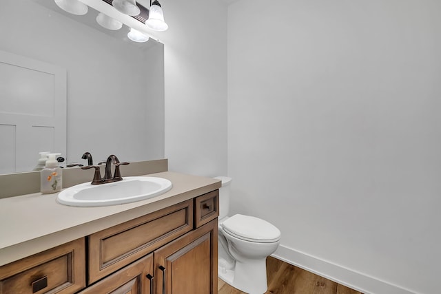 half bathroom featuring baseboards, vanity, toilet, and wood finished floors