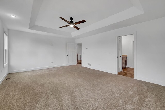 carpeted empty room with ceiling fan and a raised ceiling