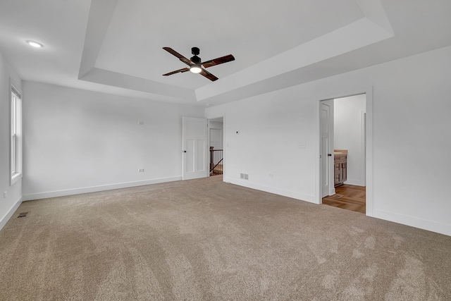 unfurnished bedroom featuring ceiling fan, carpet flooring, visible vents, baseboards, and a tray ceiling