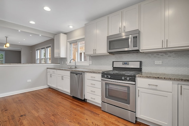 kitchen featuring white cabinets, light wood-type flooring, light stone countertops, and stainless steel appliances