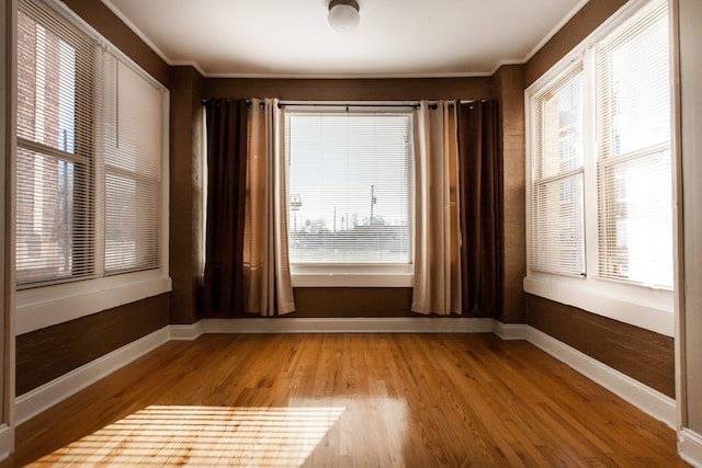 empty room with plenty of natural light, crown molding, and wood-type flooring