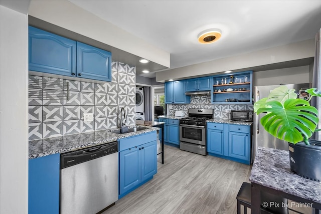 kitchen with blue cabinets, sink, backsplash, stacked washer / dryer, and stainless steel appliances