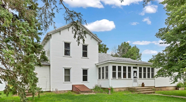 rear view of house featuring a shingled roof, a lawn, and a sunroom