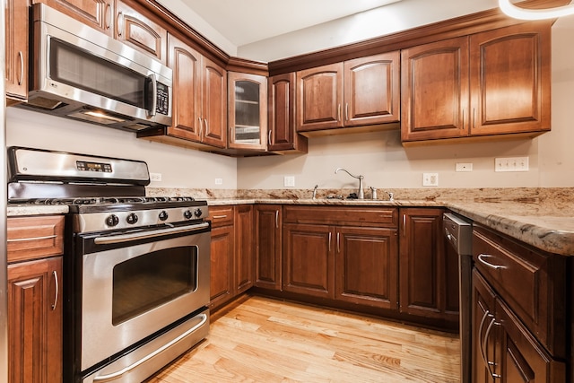 kitchen with appliances with stainless steel finishes, sink, light wood-type flooring, and light stone countertops