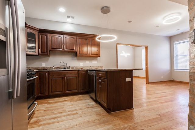 kitchen featuring appliances with stainless steel finishes, hanging light fixtures, sink, and light hardwood / wood-style floors