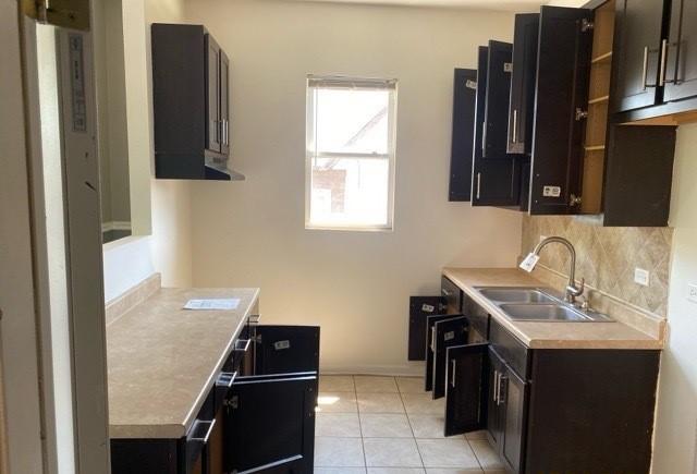 kitchen with dark brown cabinets, sink, light tile patterned floors, and decorative backsplash