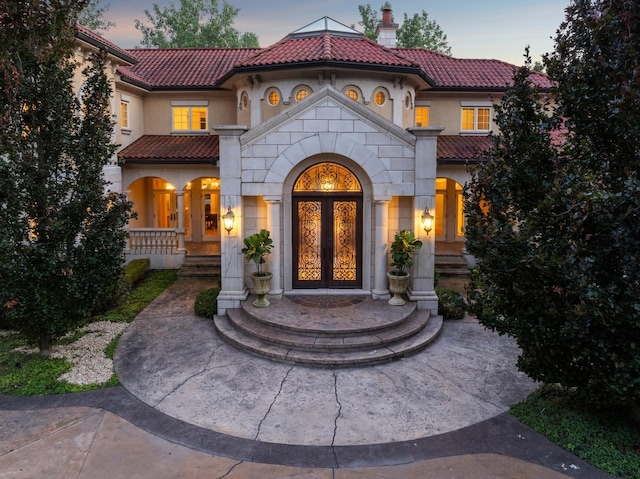 view of exterior entry with stucco siding, a chimney, french doors, stone siding, and a tiled roof