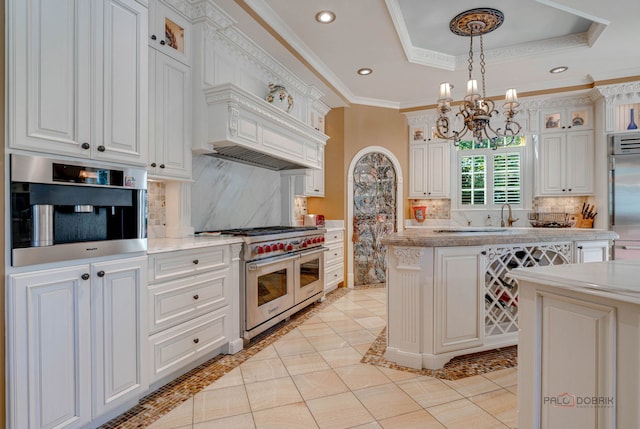 kitchen with a tray ceiling, ornamental molding, light countertops, glass insert cabinets, and premium appliances