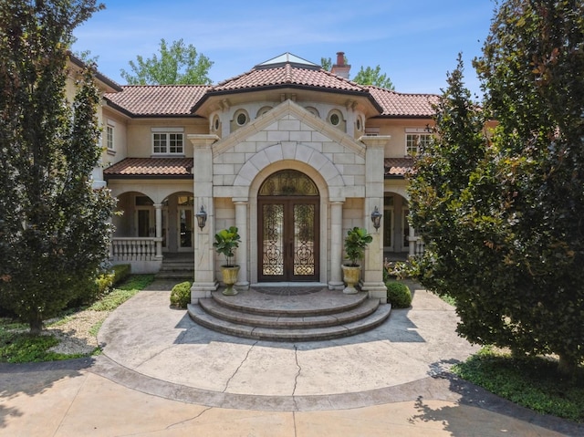 exterior space with a tile roof, stucco siding, french doors, a chimney, and stone siding