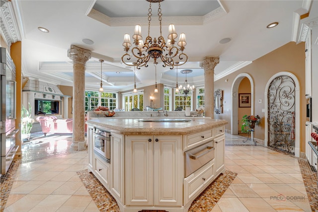 kitchen with a tray ceiling, cream cabinetry, decorative columns, and a chandelier