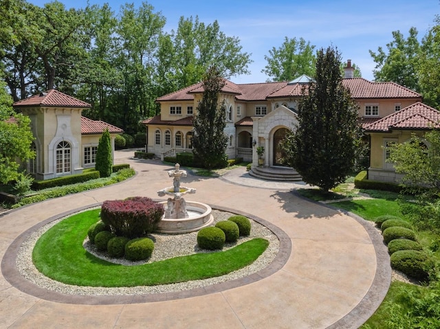 mediterranean / spanish home featuring stucco siding, a chimney, curved driveway, stone siding, and a tile roof