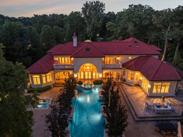 back of property at dusk featuring a chimney, a patio, a tile roof, and a balcony