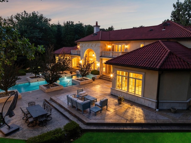 back of house featuring a jacuzzi, an outdoor pool, a balcony, a chimney, and a patio area