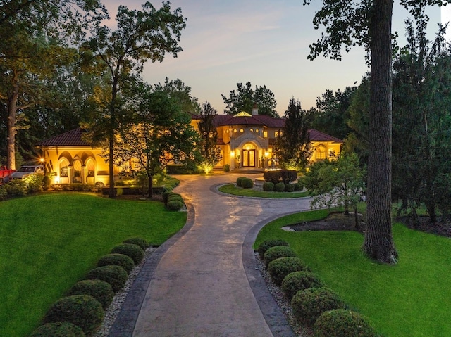 mediterranean / spanish-style house with a tile roof, decorative driveway, a yard, and a chimney