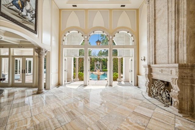 entrance foyer with french doors, arched walkways, a fireplace, a towering ceiling, and ornate columns