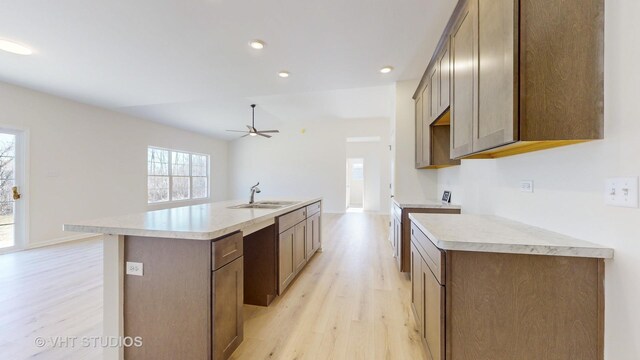 kitchen with sink, light hardwood / wood-style flooring, ceiling fan, and a kitchen island with sink