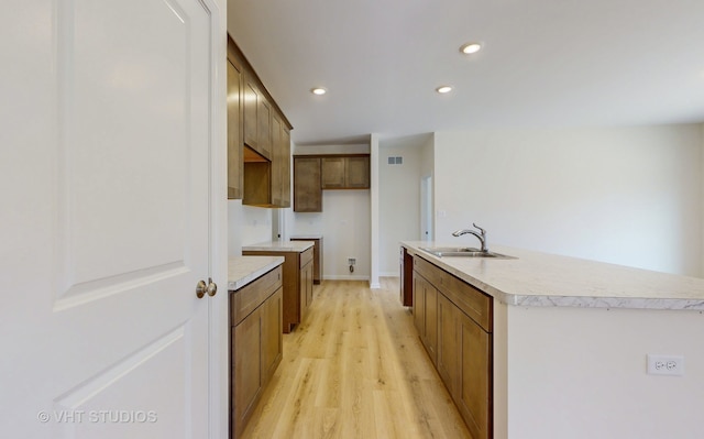 kitchen featuring sink, light wood-type flooring, and a kitchen island with sink