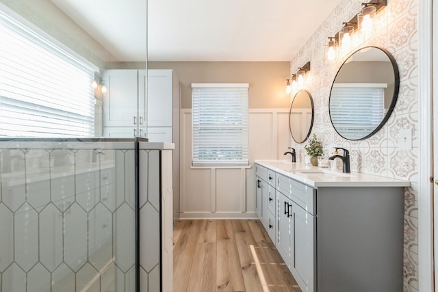 full bathroom featuring double vanity, a decorative wall, a sink, and wood finished floors