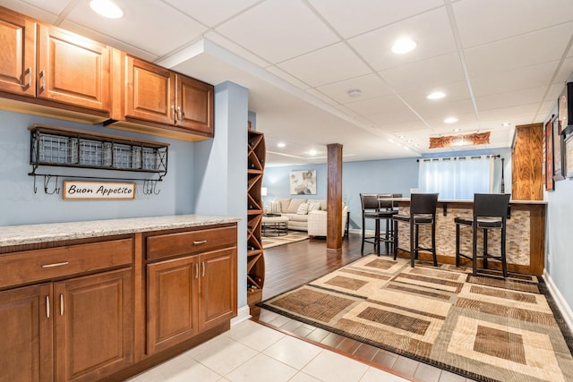 kitchen featuring light tile patterned flooring, a paneled ceiling, recessed lighting, baseboards, and brown cabinets