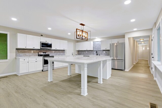 kitchen with appliances with stainless steel finishes, light hardwood / wood-style flooring, white cabinetry, and pendant lighting