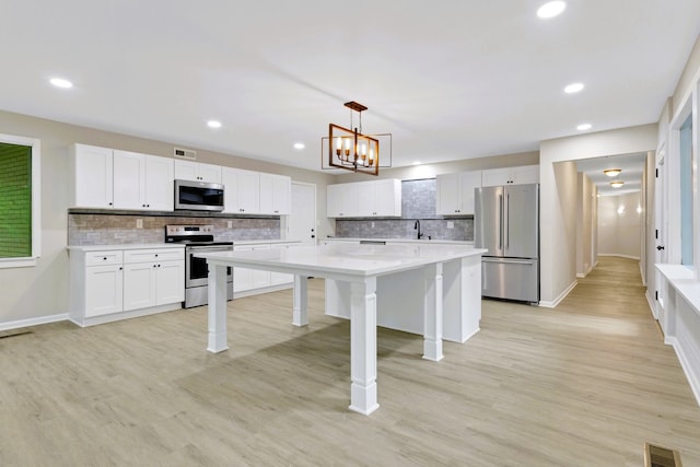 kitchen featuring stainless steel appliances, decorative light fixtures, a kitchen island, and white cabinets