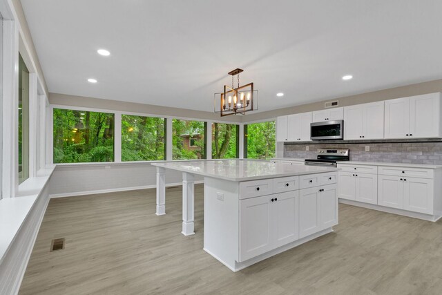 kitchen with hanging light fixtures, white cabinetry, appliances with stainless steel finishes, light hardwood / wood-style floors, and tasteful backsplash