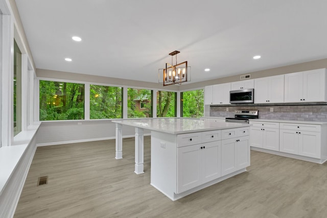 kitchen featuring a kitchen island, appliances with stainless steel finishes, pendant lighting, white cabinetry, and light hardwood / wood-style floors