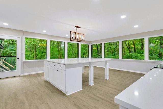 kitchen with a wealth of natural light, white cabinetry, hanging light fixtures, and light hardwood / wood-style floors