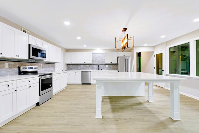 kitchen with appliances with stainless steel finishes, a breakfast bar, white cabinets, and decorative light fixtures